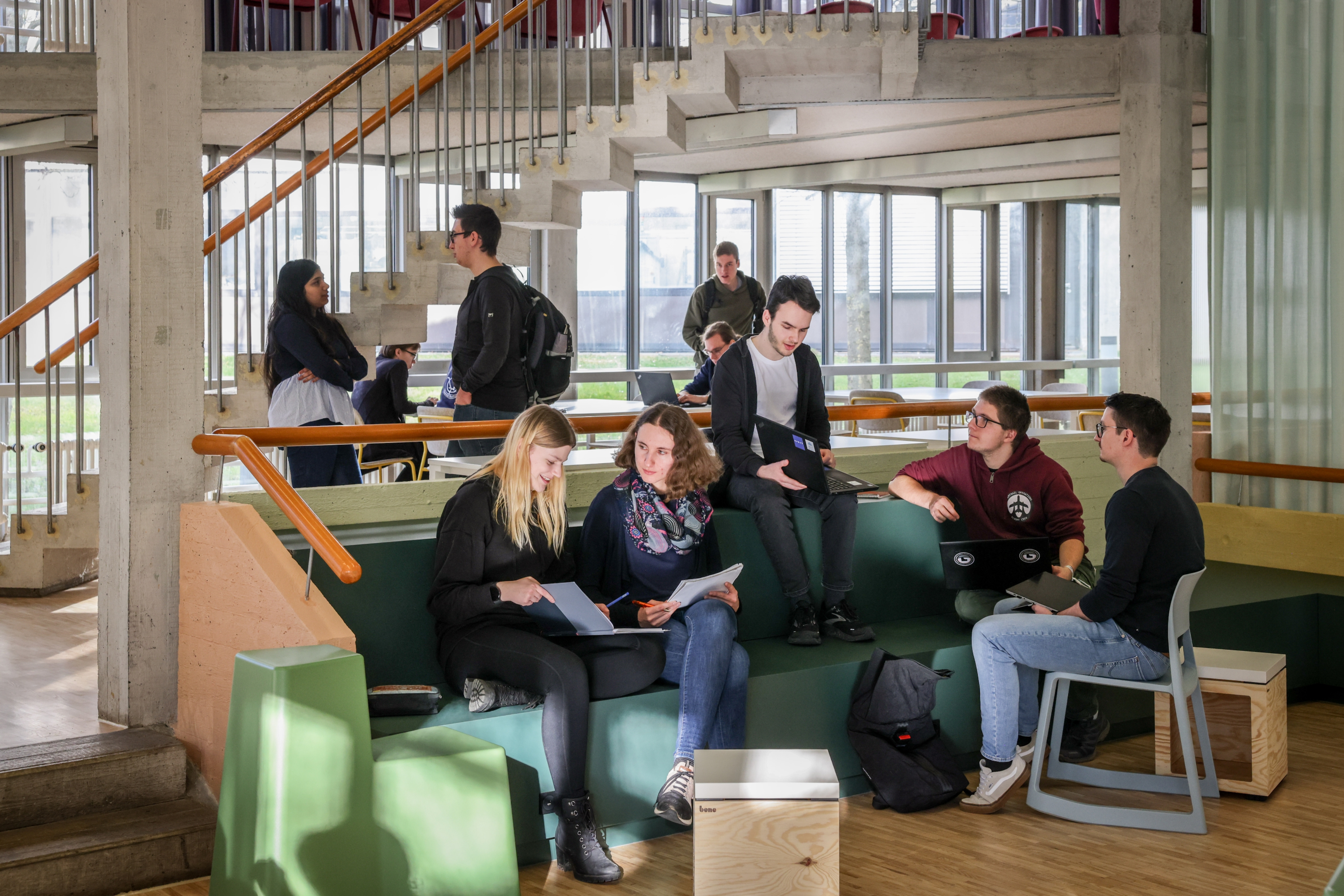 Der neue helle Lernraum, eine Gruppe Studierender sitzt zusammen, schaut auf Bildschirme und Notizblöcke und unterhält sich.